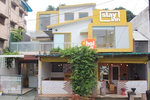 Ein zweistöckiges Gebäude mit einem 'Stay Inn'-Schild und einem Schild für 'Chai'. Im oberen Stock sind zwei Fenster und im Erdgeschoss eine Tür zu sehen.