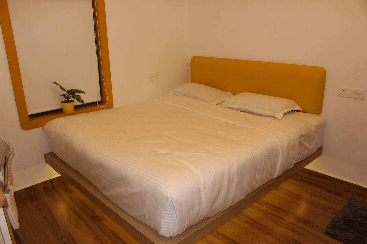 Un letto con struttura in legno, una testiera gialla e un materasso bianco.