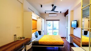 A compact hotel room with a bed, a desk, a chair, a TV, a ceiling fan, and a window. - Stay Inn (Bhopal)