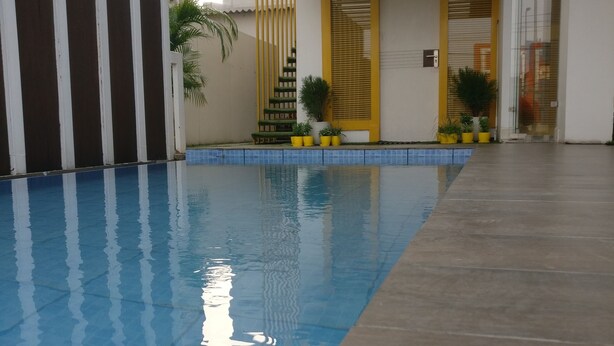 A swimming pool with a tiled edge, a staircase with yellow railings, and potted plants. - Stay Inn (Bhopal)