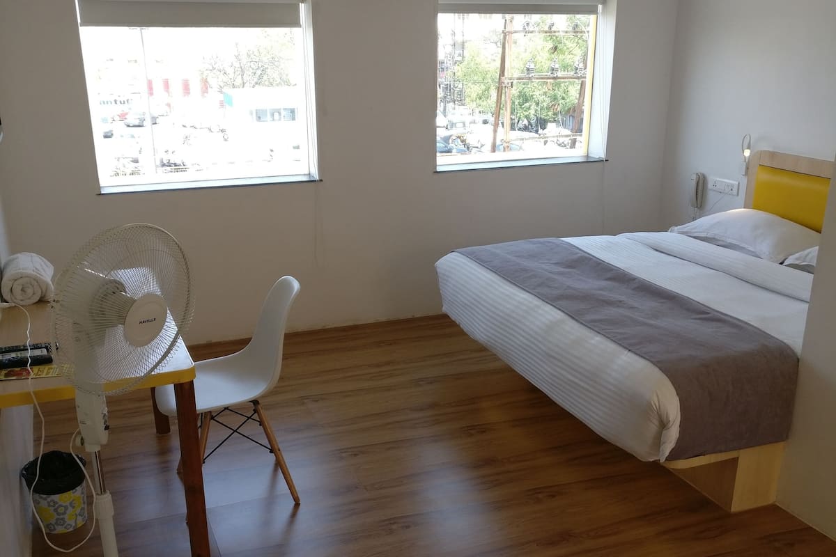 Una camera da letto con un letto, una scrivania con una sedia, un condizionatore d'aria e due finestre.