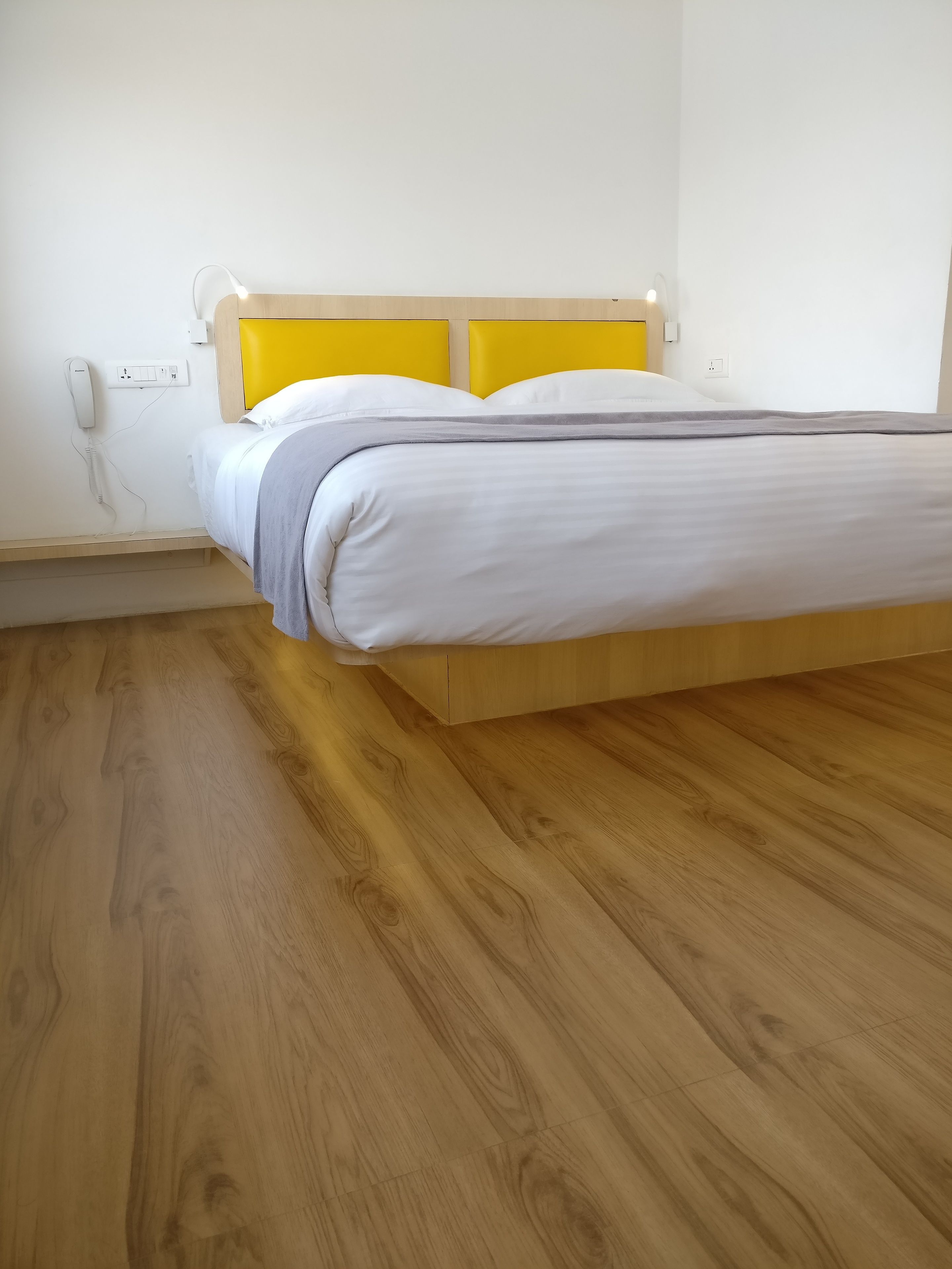 A single bed with a wooden headboard and a white mattress, a bedside telephone, and a wooden floor.