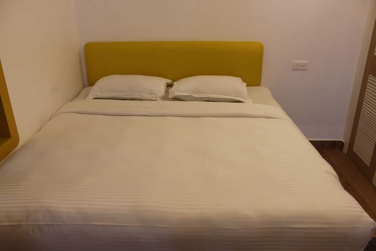 Un letto singolo con una testiera gialla, biancheria da letto bianca e una parete bianca.
