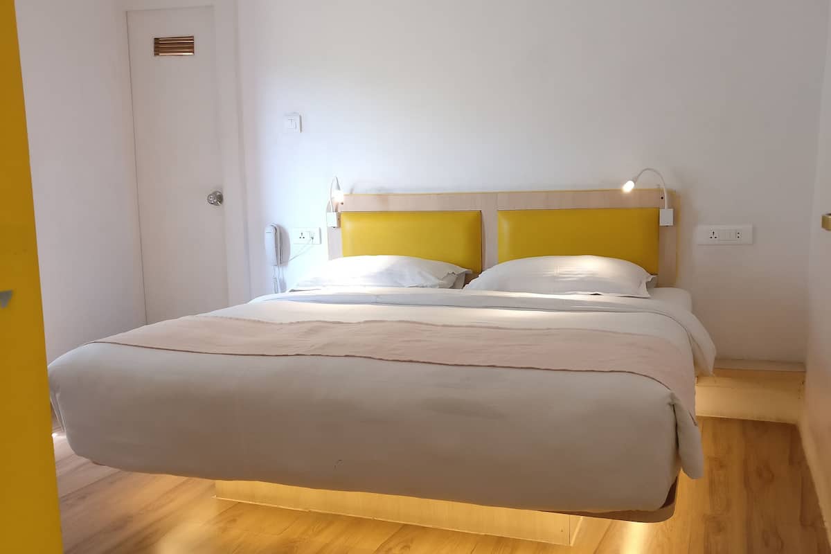Un letto con una testiera in legno e un comodino, una porta bianca e un interruttore a parete.