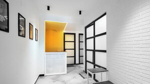 A hallway with white brick walls, a reception desk with a yellow accent, and a small table. - Stay Inn (Bhopal)