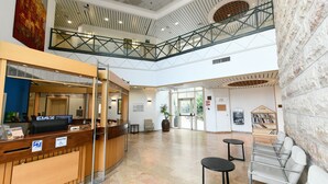 A hotel lobby with a reception desk, seating area, and a staircase connecting two floors. - HI Agron Jerusalem Hostel (Jerusalem)