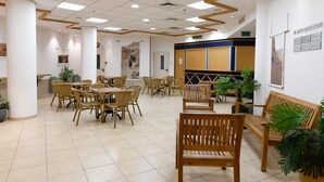 A spacious indoor area with multiple wooden tables and chairs, a wooden bench, and potted plants. - HI Agron Jerusalem Hostel (Jerusalem)
