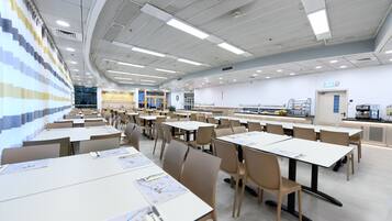 Una amplia sala de conferencias con varias mesas y sillas, equipada con iluminación incorporada y un gran ventanal.
