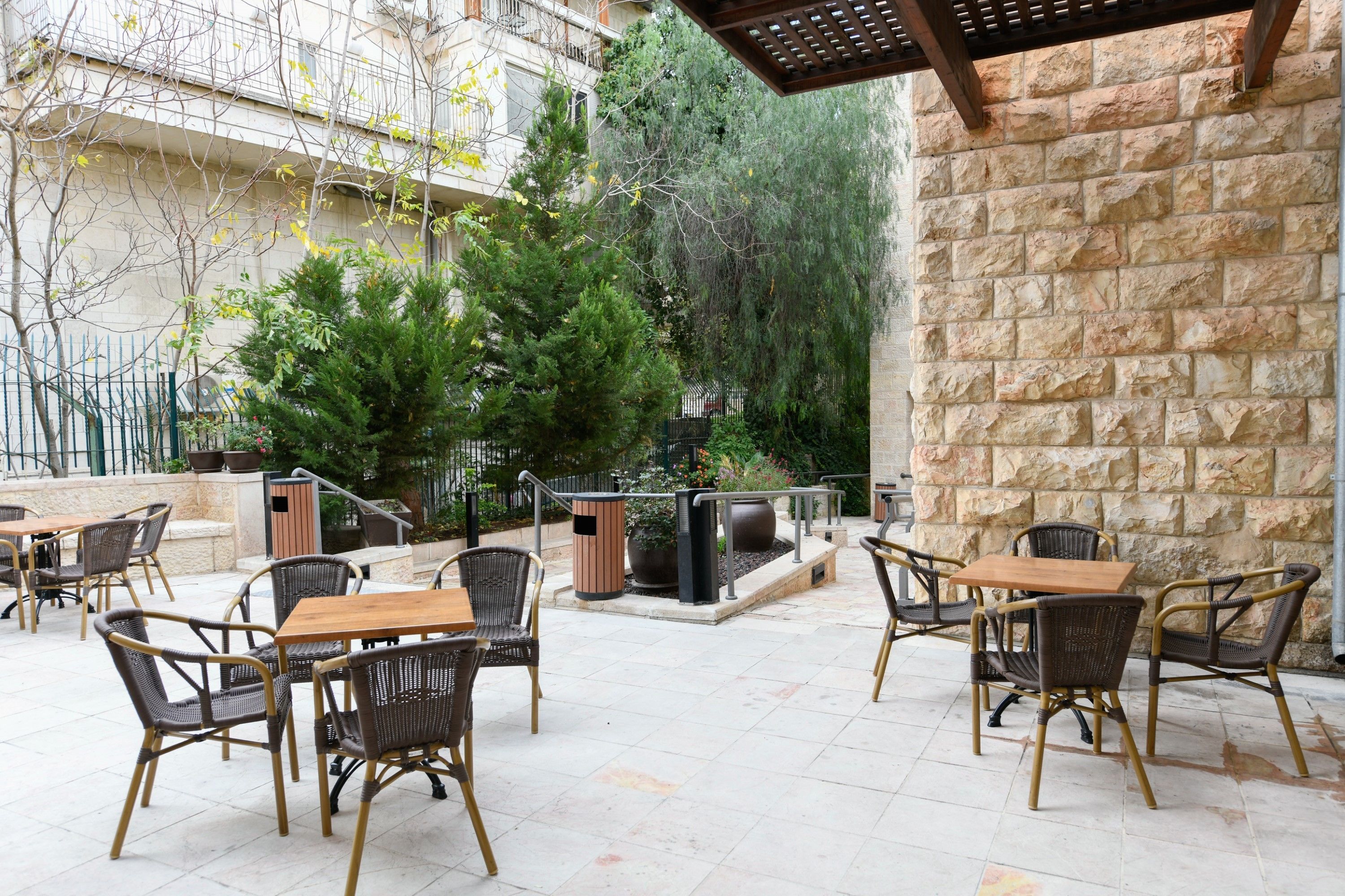 An outdoor patio with stone walls, wicker furniture, and a fire feature. - HI Agron Jerusalem Hostel (Jerusalem)