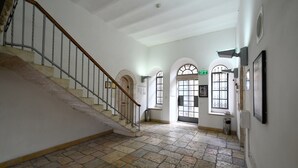 A spacious hallway with a stone floor, a wooden staircase, and arched doorways. - HI Agron Jerusalem Hostel (Jerusalem)