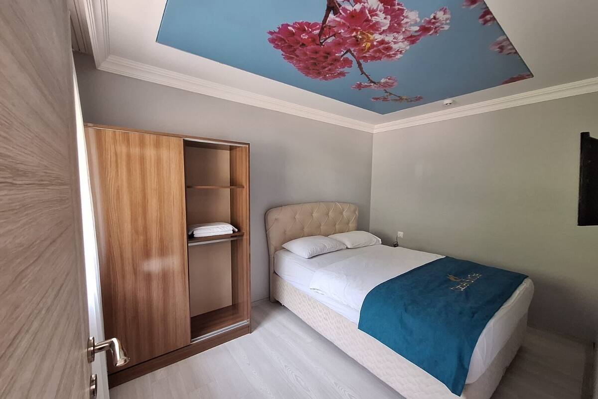 Un dormitorio con una cama, un armario y un mural floral rosa en el techo.
