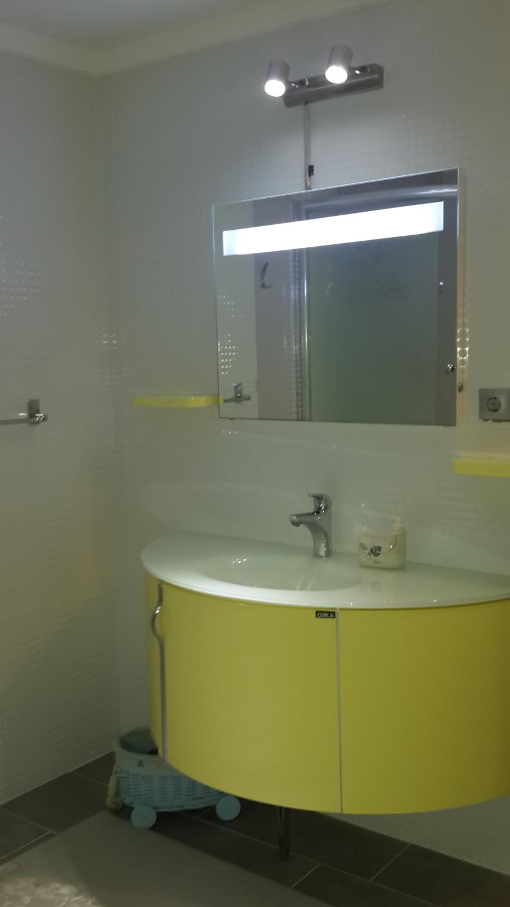 Un baño con tocador amarillo, espejo y lavamanos.