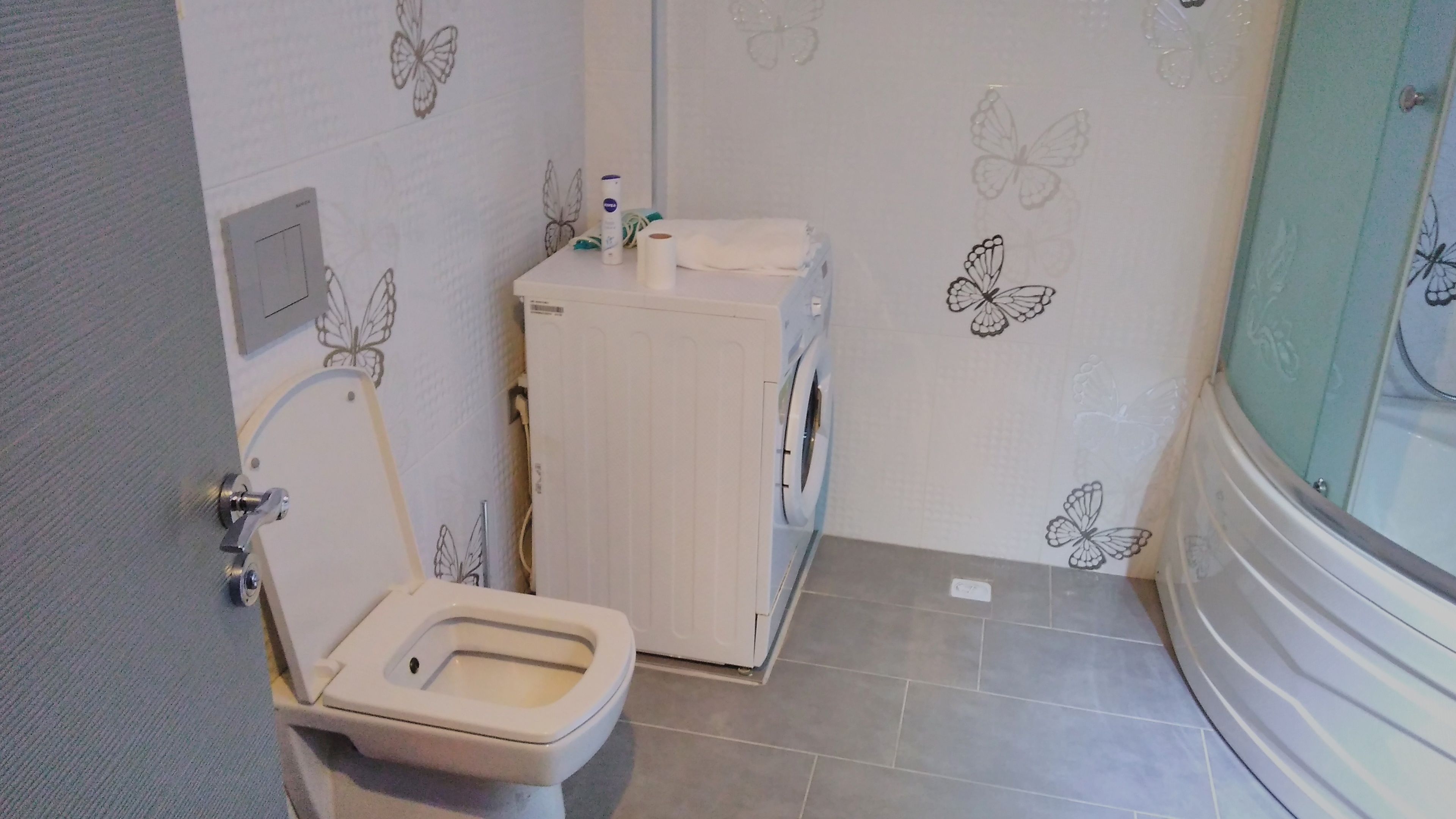 A small bathroom with a toilet, a washing machine, and a shower area.