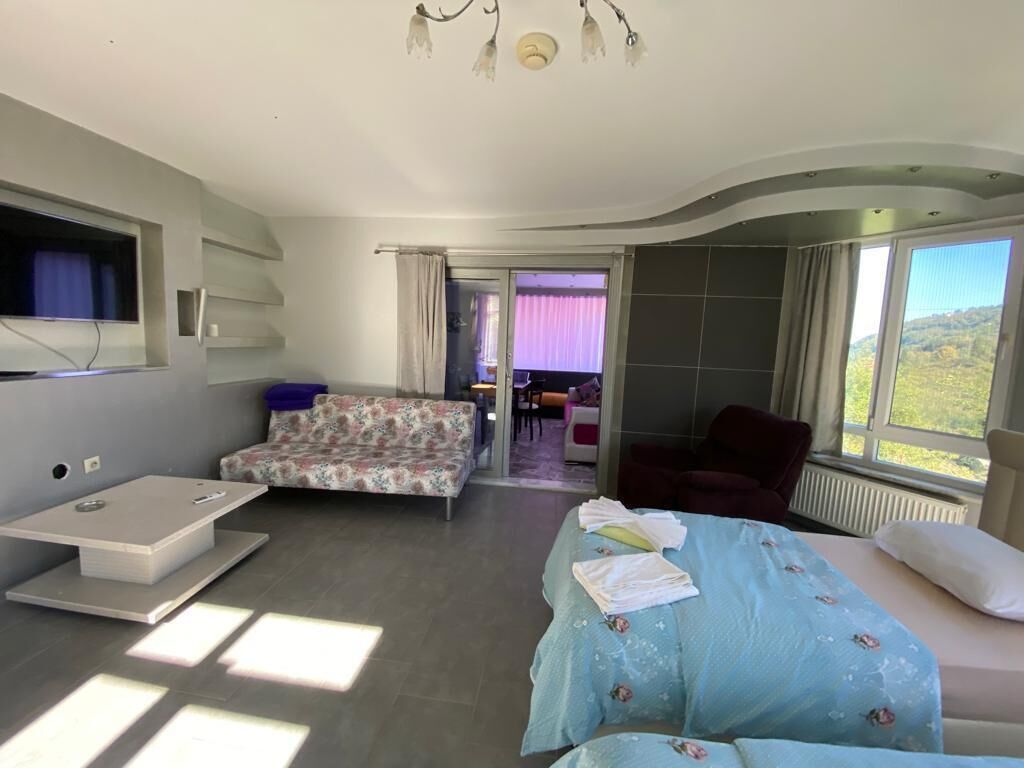 A modern bedroom with a bed, a sofa, and a TV. There is a view of the outdoors through the window.