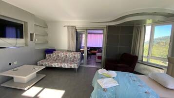 A modern bedroom with a bed, a sofa, and a TV. There is a view of the outdoors through the window.