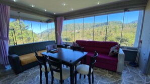 A room with a dining table, chairs, a red sofa, and a view of a mountainous landscape through large windows. - Cosy Park Apartment (Yomra)