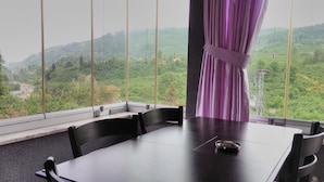 A dining area with a table and chairs, a view of a mountainous landscape through large windows, and a curtain tied to the window frame. - Cosy Park Apartment (Yomra)