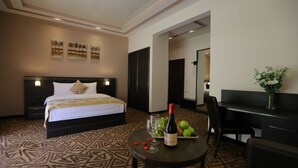 Habitación de hotel con cama, escritorio, silla, mesita con una botella y vasos, y frutero.