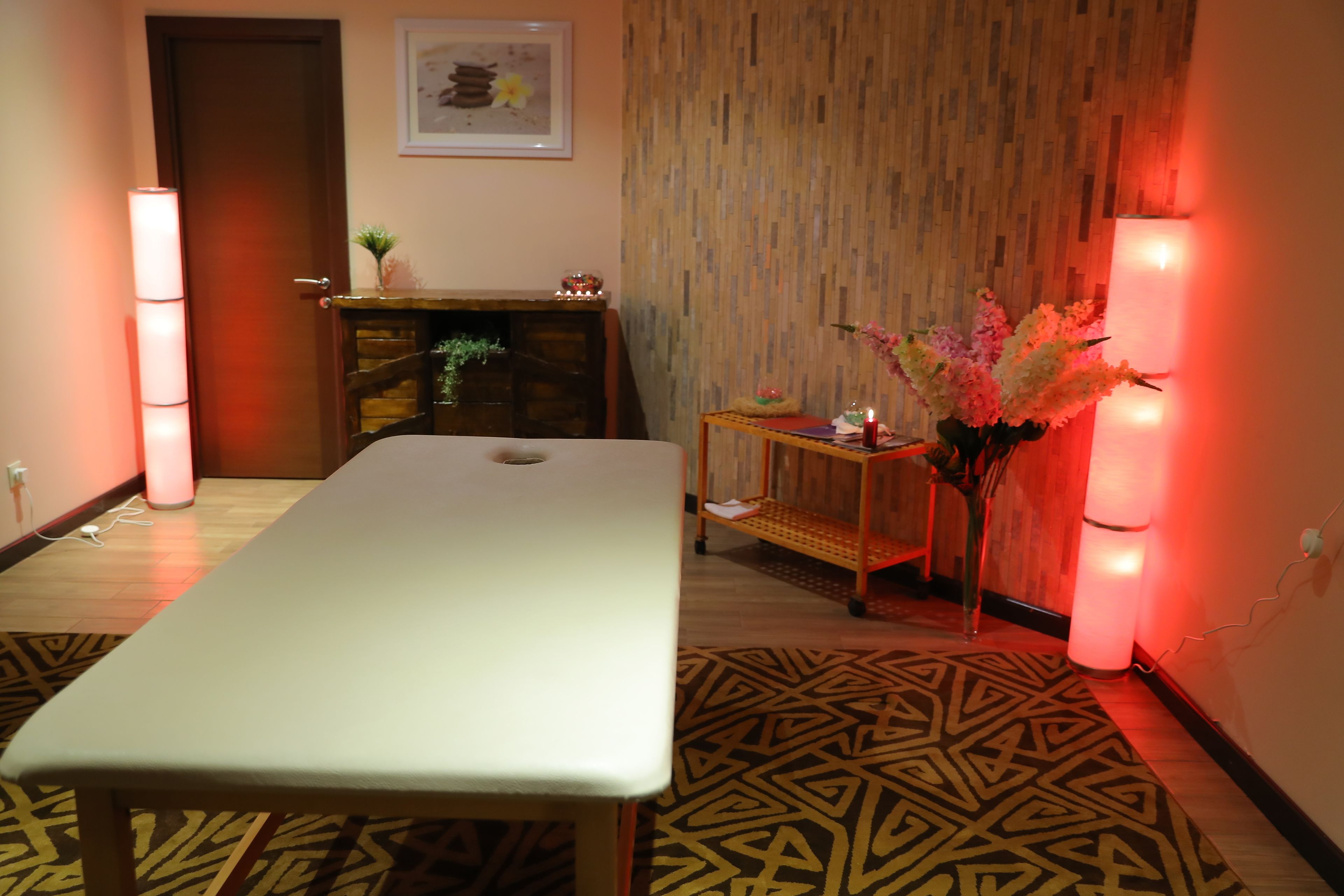 Een kamer met een lange tafel, een klein houten kastje, een tapijt met een patroon en een wand met een verticale houten paneel.
