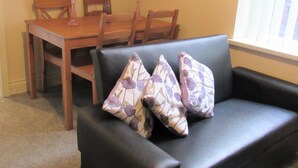 Un soggiorno con un divano nero, due cuscini decorati, un tavolo da pranzo in legno e sedie.