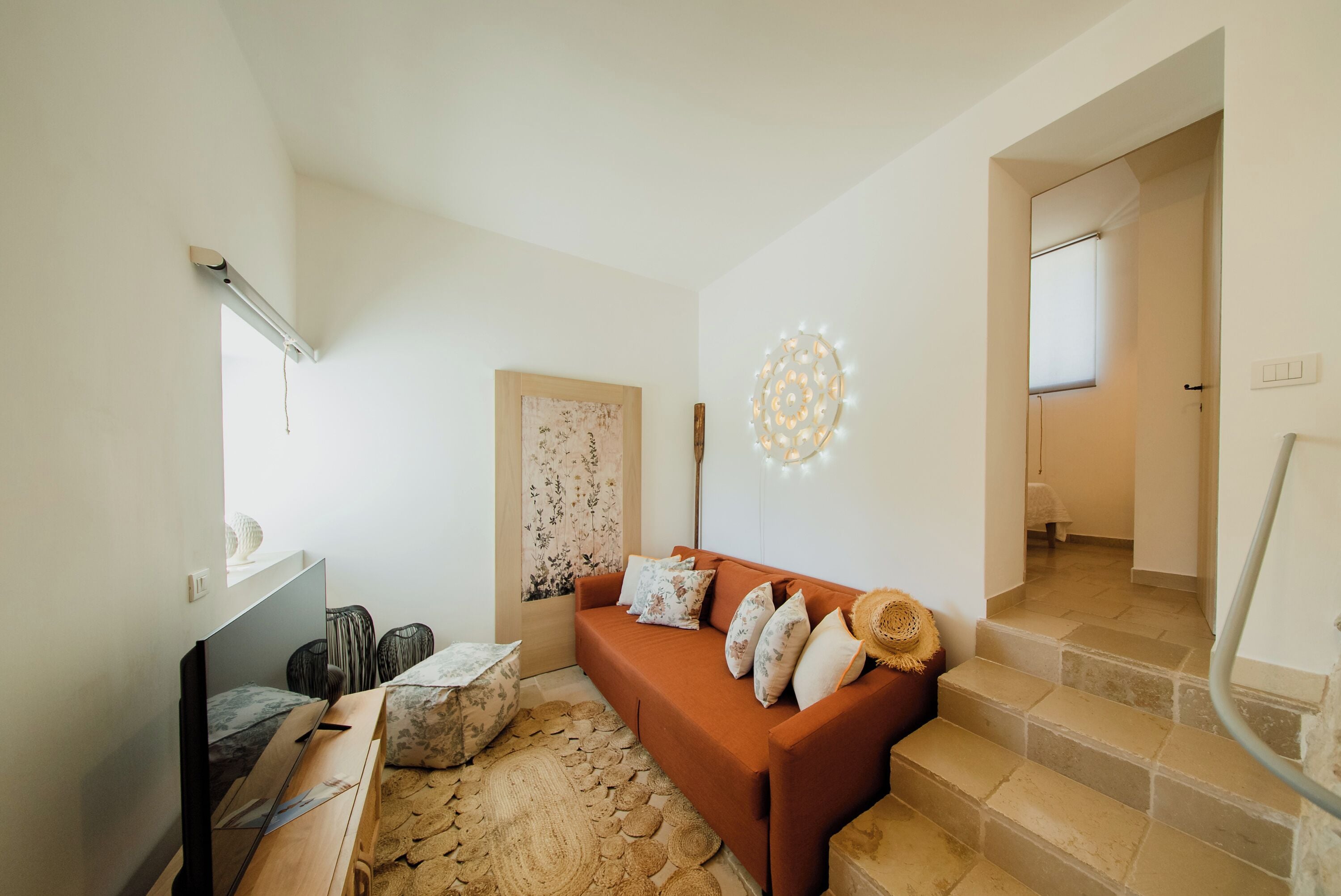 A living room with a sofa, a flat-screen TV, a decorative wall light, and a staircase leading to another room.