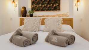 Una cama bien hecha con toallas enrolladas, un adorno en la pared y luces fijadas a la pared.