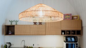 Una cocina con lámpara de fibra trenzada, armarios de madera, microondas y lavamanos.