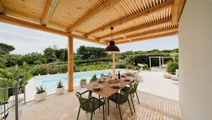 Un patio al aire libre con piscina, pérgola de madera, suelo de piedra y sillas verdes.