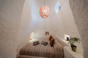 Una habitación acogedora, con techos altos, una cama, almohadas, una planta en maceta y una lámpara colgante.