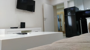 Ein modernes Hotelzimmer mit einem an der Wand montierten Flachbildfernseher, einem weißen Konsolentisch und einem schwarzen Kühlschrank.