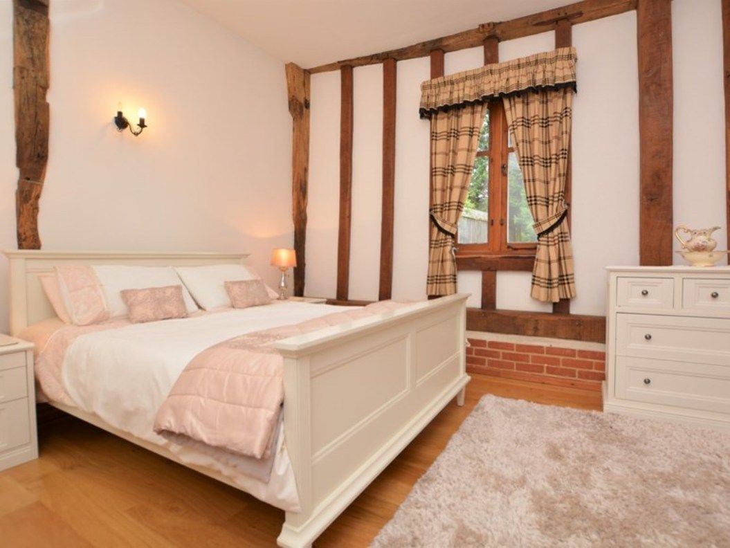 A bedroom with a large bed, a nightstand, a dresser, and a window with curtains.