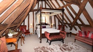 A bedroom with a four-poster bed, a red armchair, a wooden table with a lamp, and a fur rug. - Doves Barn (Ipswich)