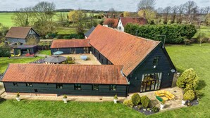 A large, dark-colored building with a sloped roof, a patio area with outdoor seating, and a well-maintained lawn. - Doves Barn (Ipswich)