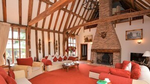 A spacious living room with a high ceiling, exposed wooden beams, a brick fireplace, and comfortable seating areas. - Doves Barn (Ipswich)