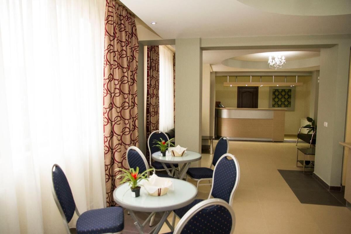 Une chambre d’hôtel dotée d’un coin repas avec des tables et des chaises rondes, d’une kitchenette et d’un couloir menant à une autre pièce.