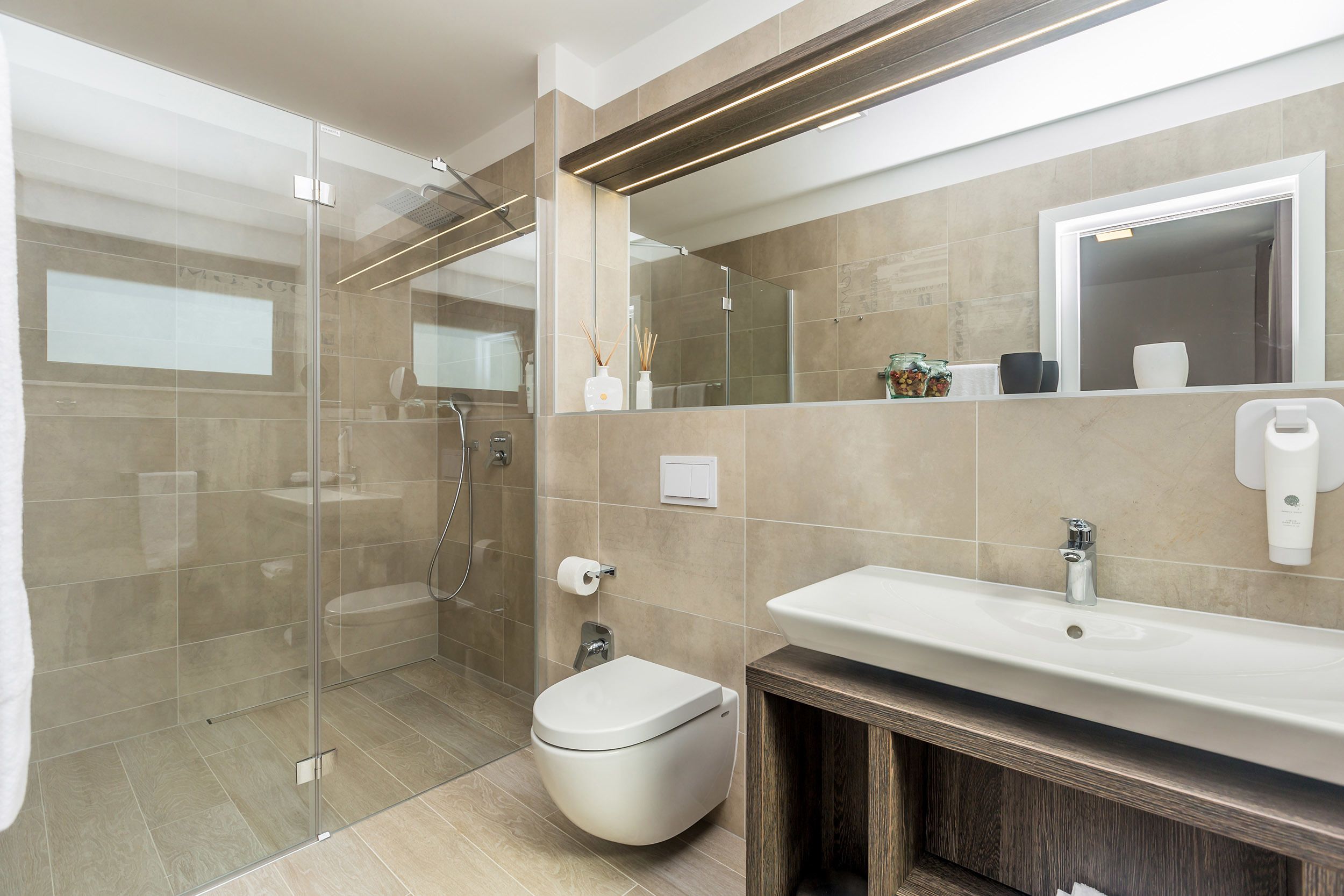A modern bathroom with a glass shower enclosure, a white toilet, a sink with a mirror above, and a wooden vanity.