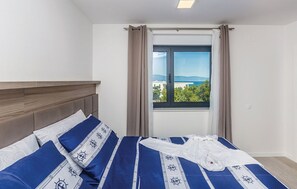 Ein Schlafzimmer mit Bett, einem Fenster mit Vorhängen und Blick ins Freie.