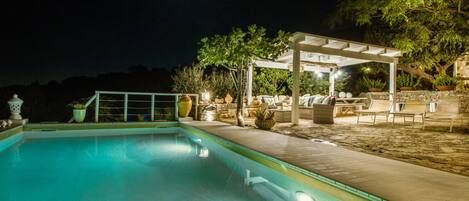 A nighttime pool area with a covered seating area and lounge chairs.