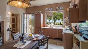 A kitchen with wooden cabinets, a dining table with chairs, a hanging light fixture, and a view through the window. - TD Casa Torchiano Hilltop Pool with Sea View (Monopoli)