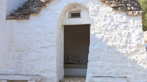 A white stone building with a small arched doorway leading to a bench with cushions. - TD Casa Torchiano Hilltop Pool with Sea View (Monopoli)