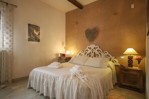 A neatly made bed with a heart-shaped wall decoration, a bedside lamp, and a small table with a vase of flowers. - TD Casa Torchiano Hilltop Pool with Sea View (Monopoli)