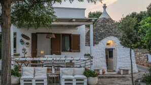 A cozy outdoor seating area with a white table and chairs, a stone-built structure with a chimney, and a garden sign. - TD Casa Torchiano Hilltop Pool with Sea View (Monopoli)
