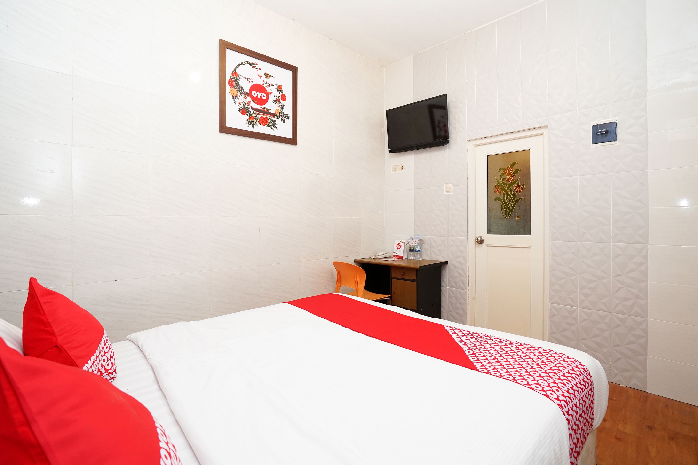 A hotel room with a bed, a desk, a TV, and a door.