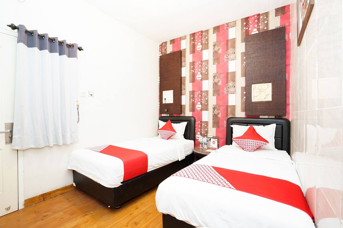 A hotel room with two beds, a wooden floor, a white door, and a patterned wall.