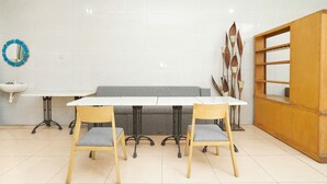 A dining area with a white table, two wooden chairs, a grey sofa, a wooden cabinet, and a blue decorative item on the wall. - Hotel O Mojokerto Guesthouse (Mojokerto)