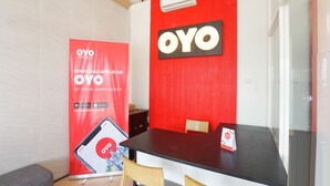 A reception area with a red wall, a black reception desk, and a large OYO Hotels promotional banner. - Hotel O Mojokerto Guesthouse (Mojokerto)