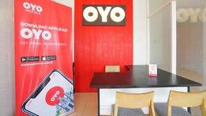 A hotel reception area with a red wall, a black reception desk, and two wooden chairs. - Hotel O Mojokerto Guesthouse (Mojokerto)