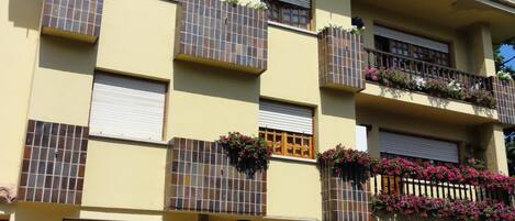 A multi-story building with balconies, some with plants and flowers.