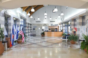 Un hall amplio con una mesa de recepción, varias banderas y plantas en macetas.