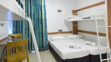 A bunk bed room with a desk and chair, a small table with a flower, and a curtain with a blue and green pattern.